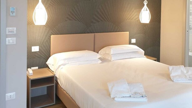 A hotel room with a large bed, two bedside tables, a nightstand, and a wall-mounted light fixture.