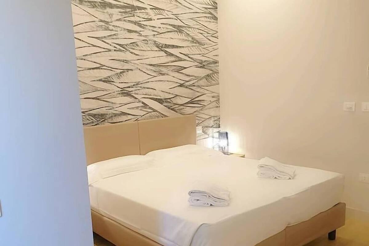 A bedroom with a bed, a glass table with a remote control, and a patterned wall.
