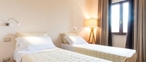 A hotel room with two beds, a lamp, a window with curtains, and a ceiling light.
