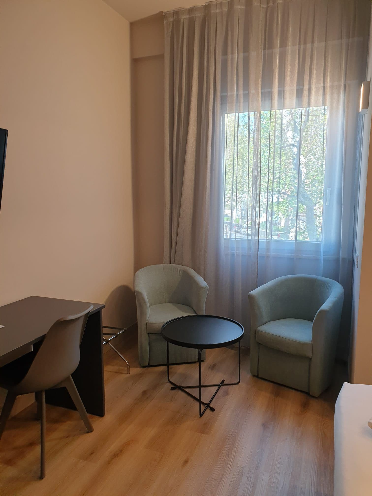 A room with a desk, two armchairs, a small round table, and a window with curtains.