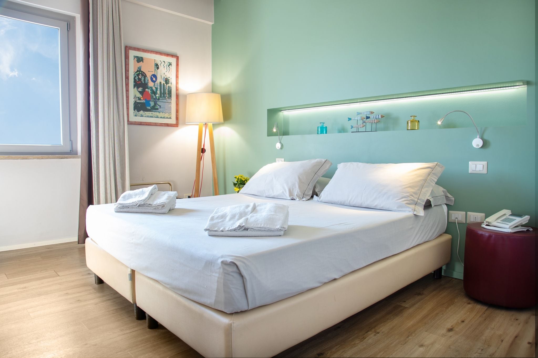 A hotel room with a bed, a bedside lamp, a telephone, and a window with curtains.