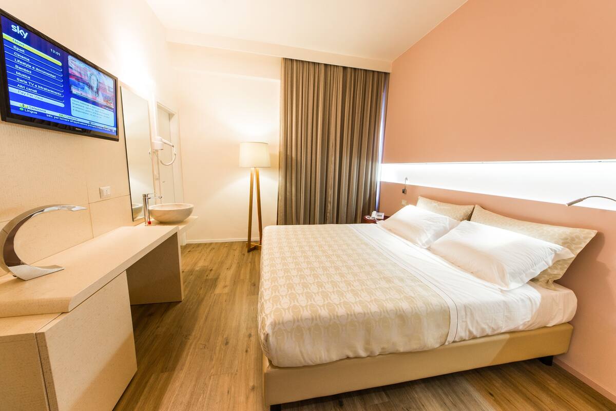 A hotel room with a bed, a desk, a mirror, a television, and a window with curtains.