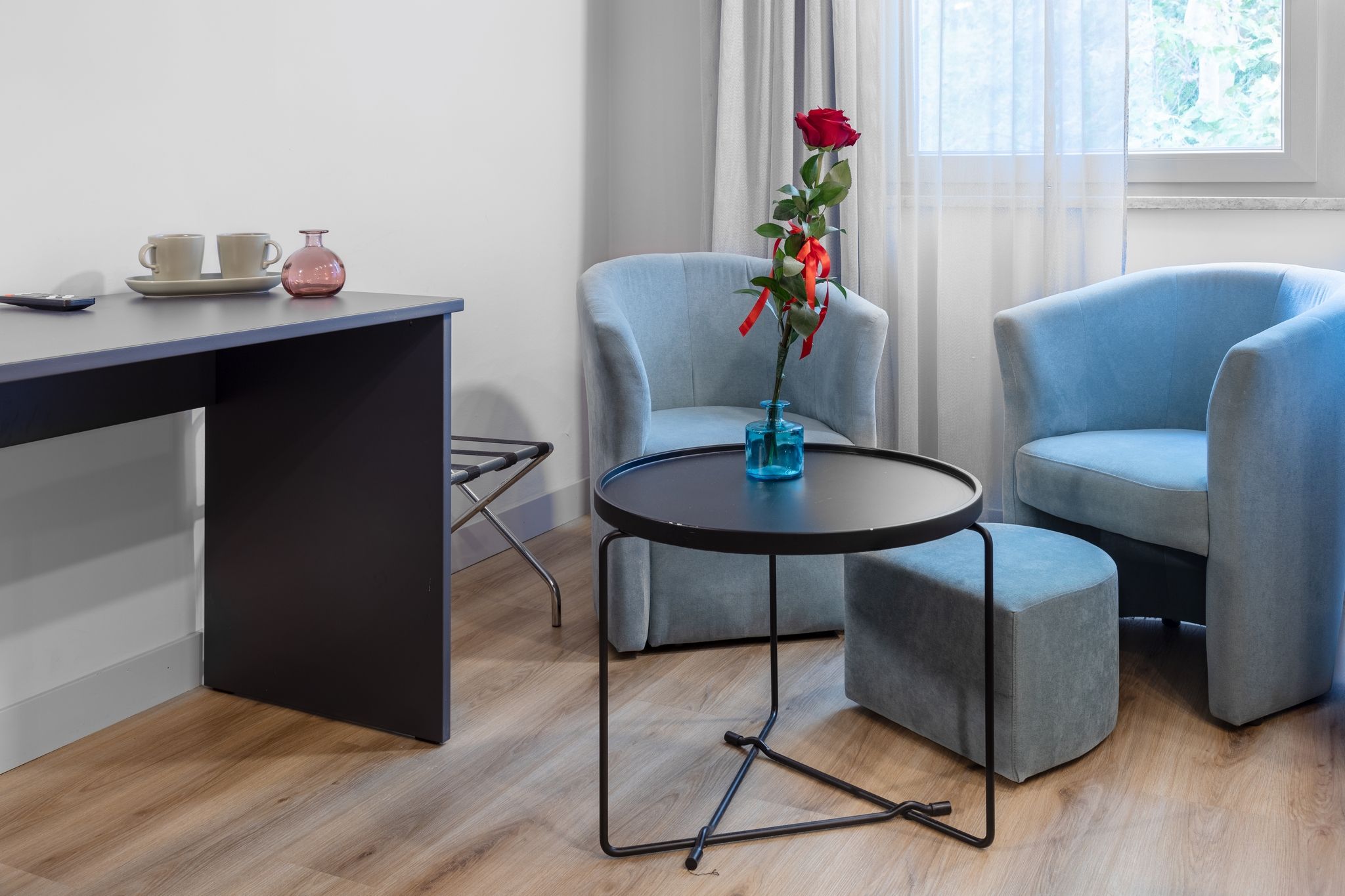 A modern room with a desk, two chairs, a small table, and a vase with a rose.