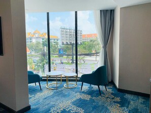 Una habitación de hotel con un ventanal grande, dos mesitas redondas pequeñas y dos sillas color turquesa.