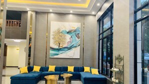 Un vestíbulo moderno con un sofá seccional azul, dos mesitas de centro doradas y un cuadro abstracto grande en la pared.