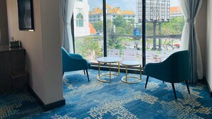 Habitación de hotel con ventanas amplias, una alfombra azul estampada, dos sillones azules y una pequeña mesa redonda.