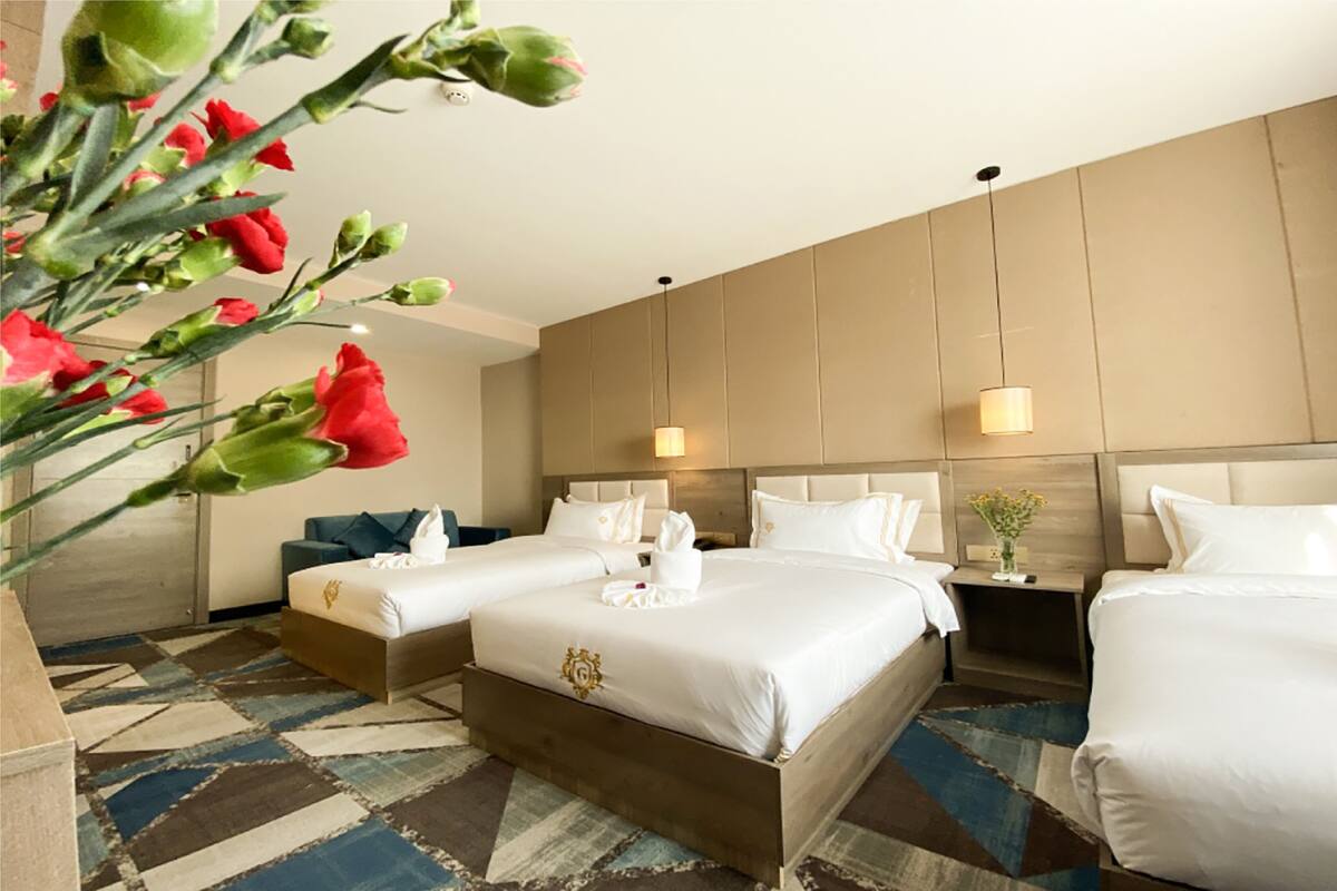A hotel room with two beds, a large window, a wooden headboard, and a decorative vase on the nightstand.