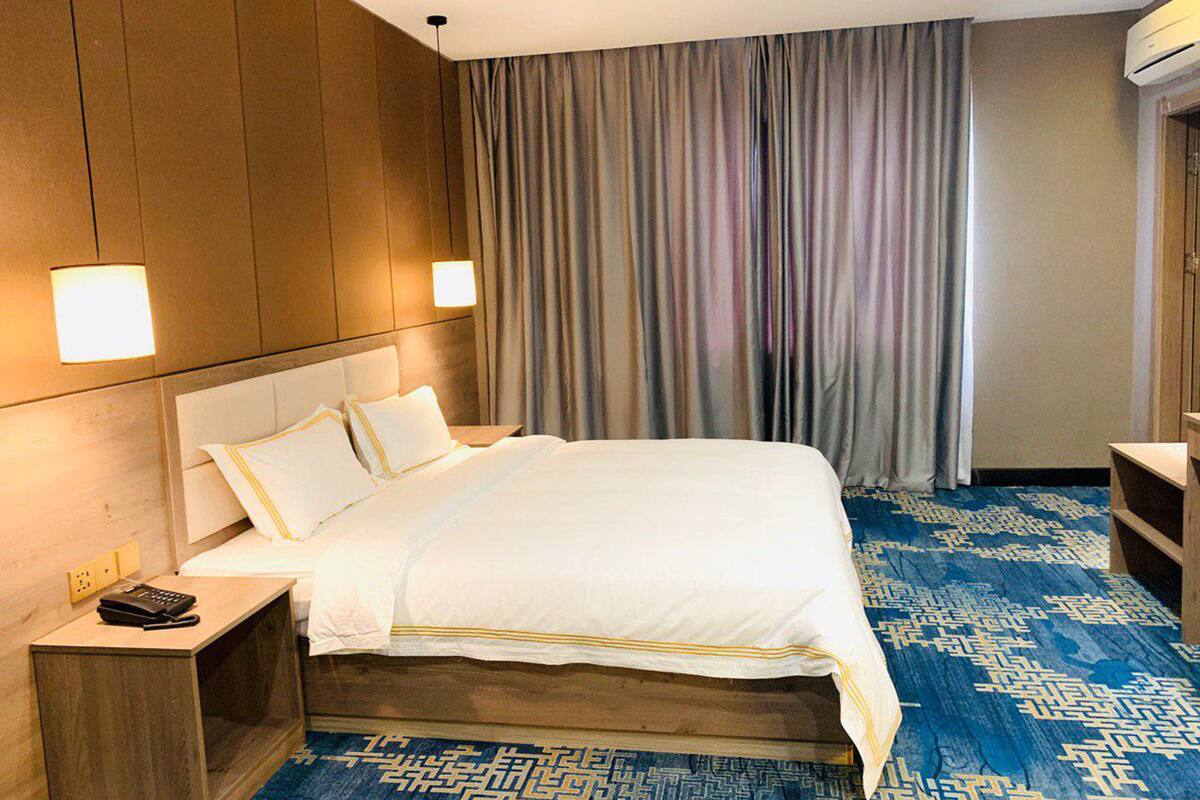 A hotel room with a large bed, wooden headboard, bedside tables, a telephone, and a patterned carpet.