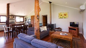 A spacious living area with a sofa, coffee table, and a fireplace. There is a dining area with chairs and a table, and a kitchen in the background. - Wildwood Valley (Yallingup)