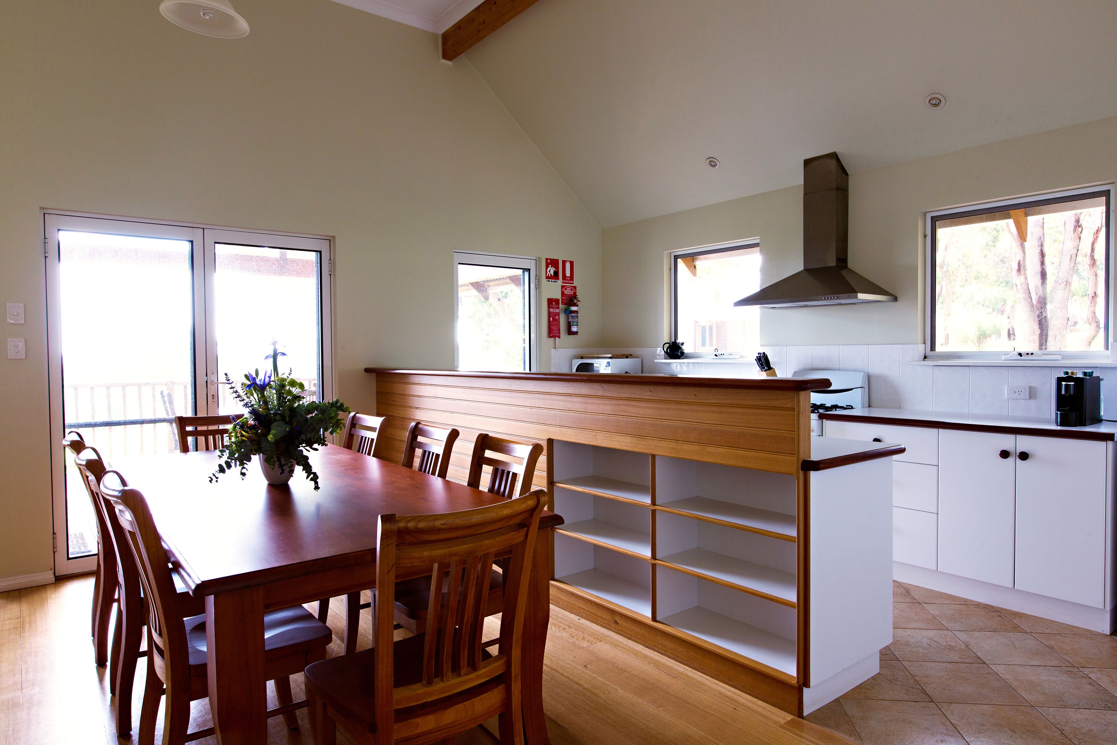 A spacious kitchen with a wooden dining table, white cabinets, and a large window.