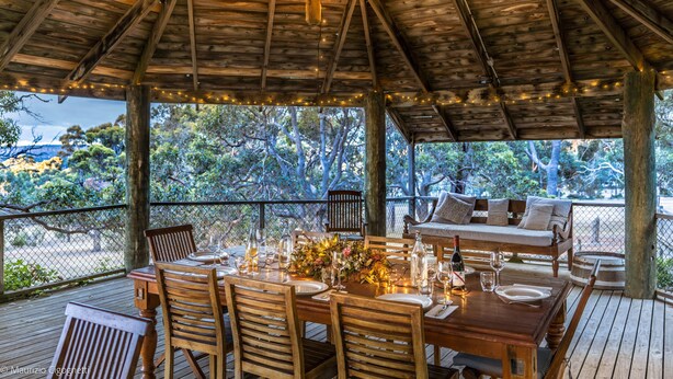 An outdoor wooden deck with a dining table set for four, surrounded by wooden chairs. - Wildwood Valley (Yallingup)