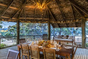 An outdoor wooden deck with a dining table set for four, surrounded by wooden chairs.