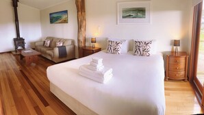 A hotel room with a large bed, a sofa, a wooden floor, a fireplace, and two paintings on the walls. - Wildwood Valley (Yallingup)