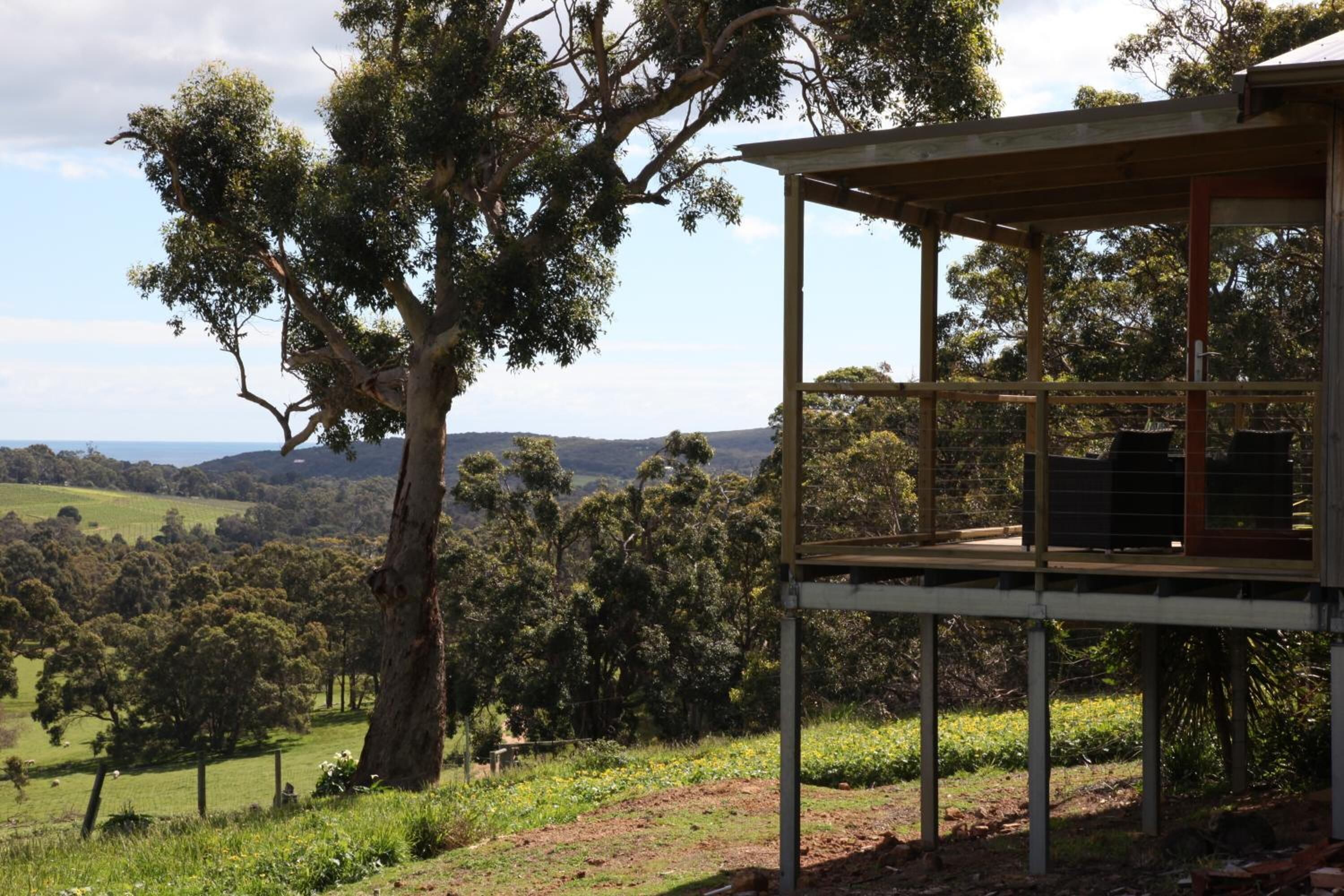 A wooden structure with a balcony overlooking a rural landscape with trees and hills.