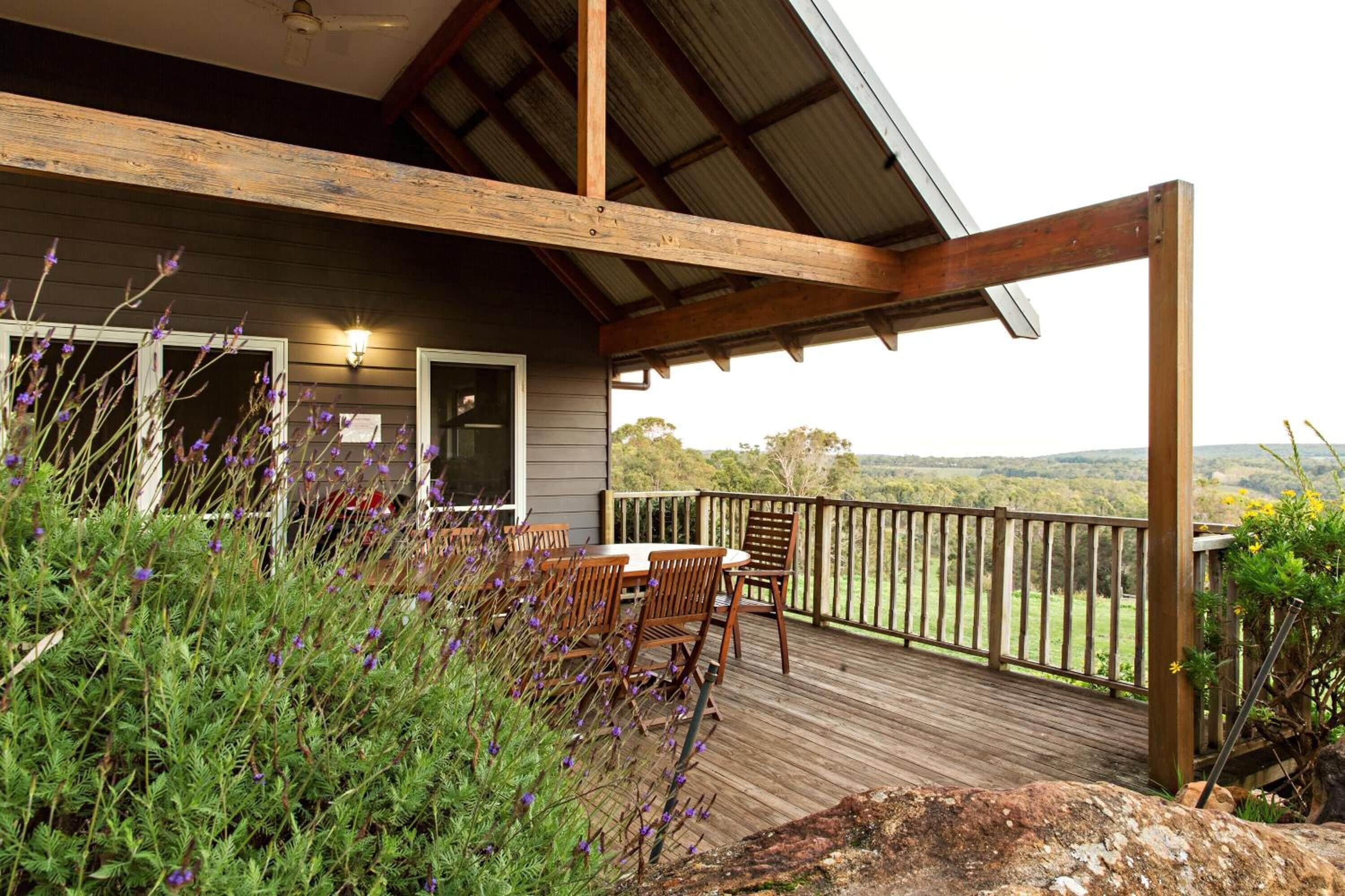 A wooden deck with outdoor seating, surrounded by vegetation and overlooking a scenic landscape.
