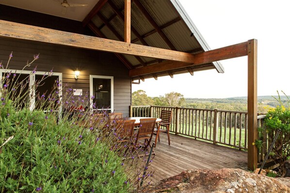 A wooden deck with outdoor seating, surrounded by vegetation and overlooking a scenic landscape.