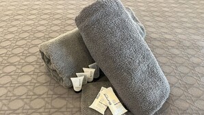 Graue Handtücher und eine Duschseife auf einem strukturierten Boden.