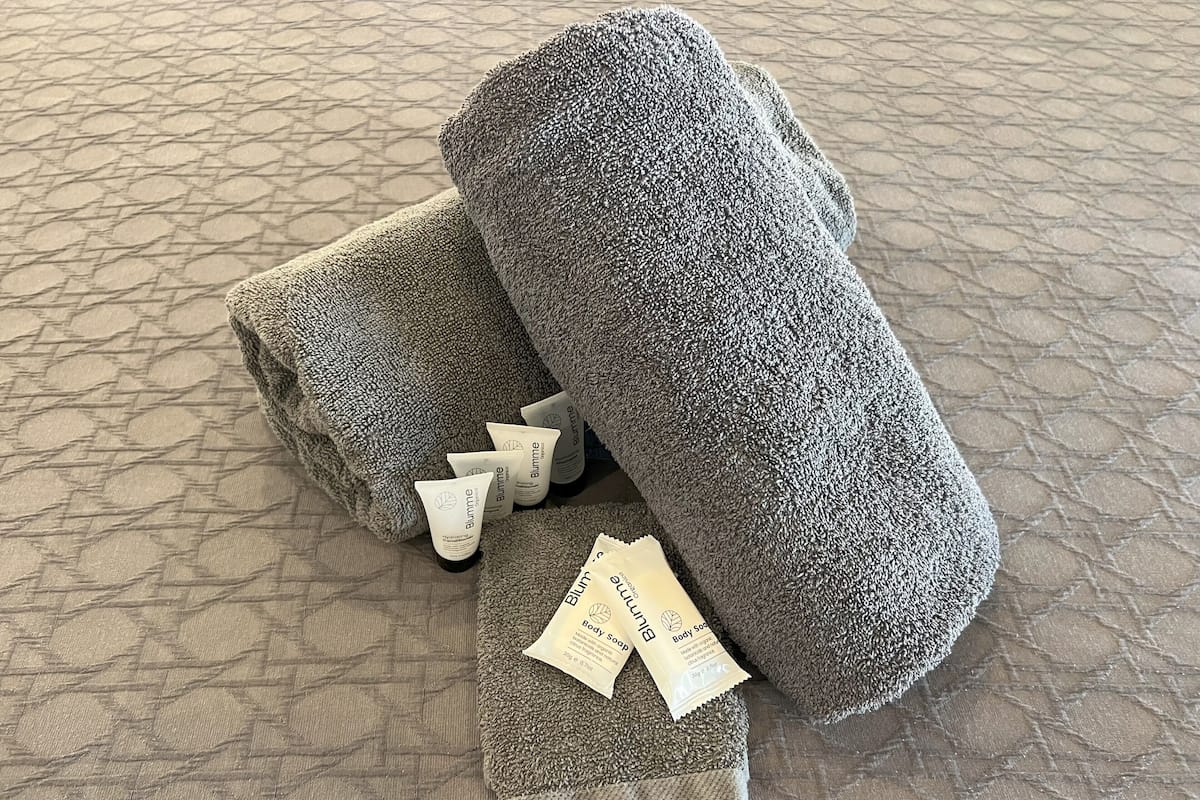 A set of grey towels and a body soap on a textured floor.