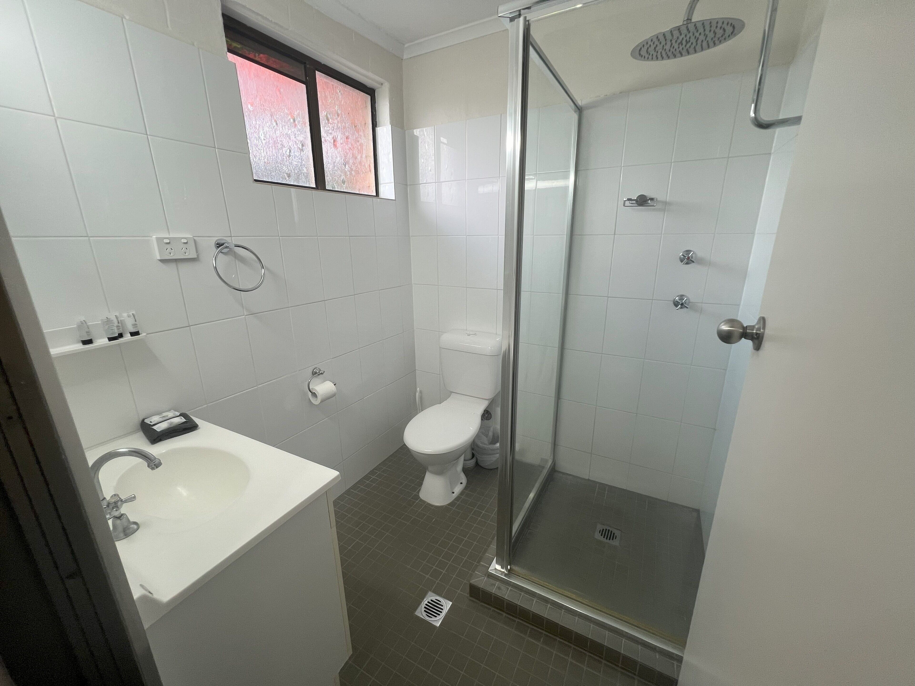 A bathroom with a shower, toilet, sink, and a window.