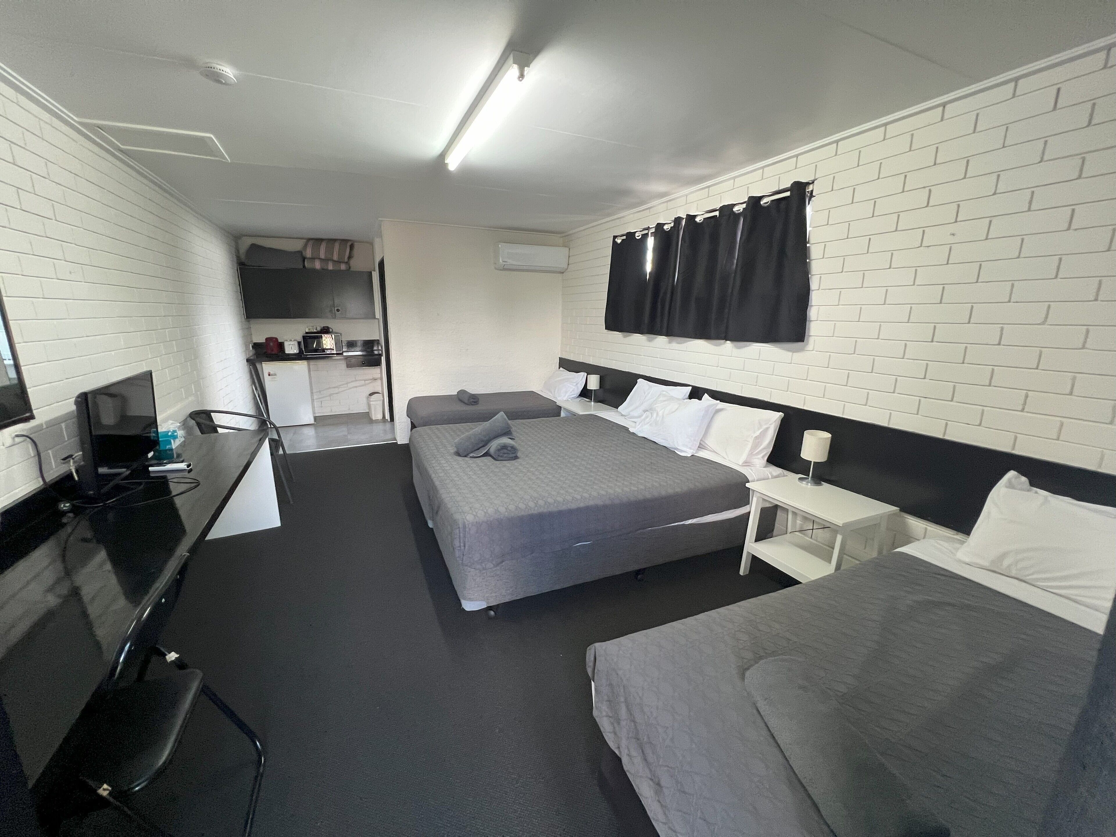 A modern hotel room with a large bed, a desk, and a kitchenette.