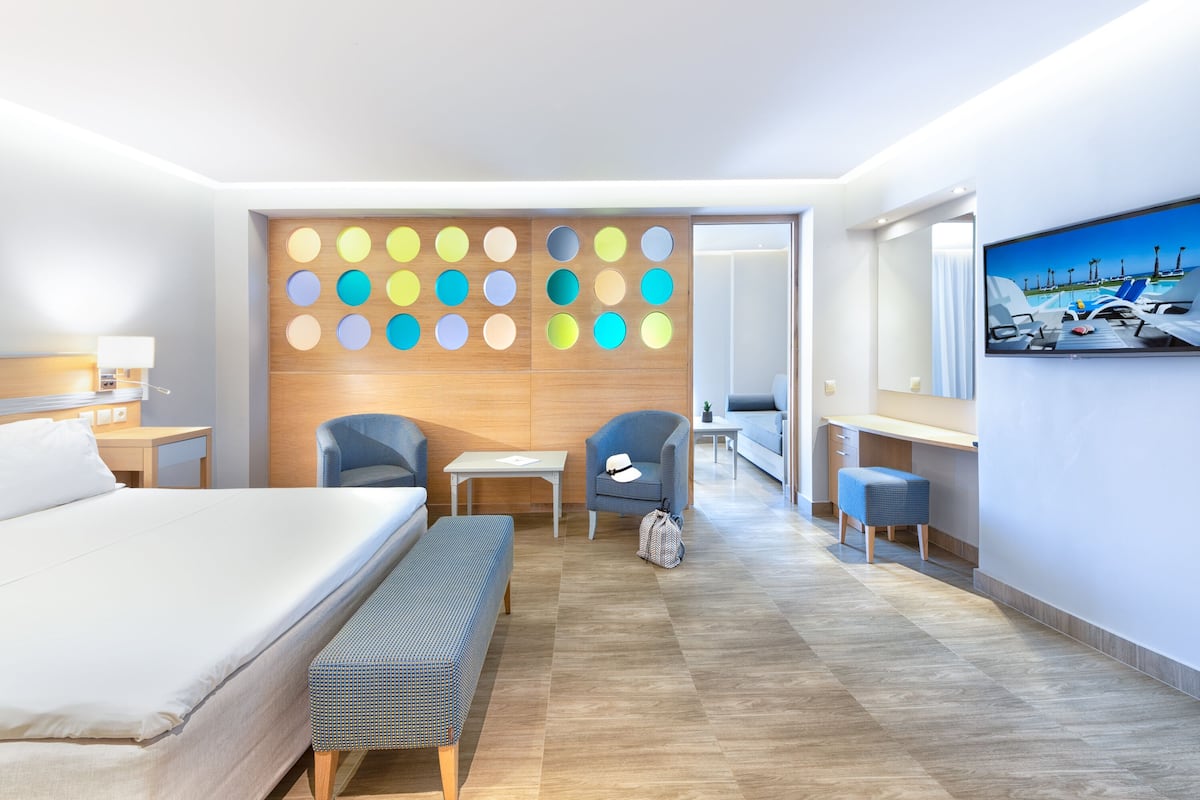 A modern hotel room with a large bed, a desk, two chairs, a bench, and a wall with colorful circular decorations.