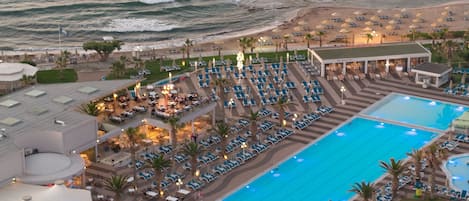 Ein Resort mit großem Schwimmbad, Strandbereich mit Liegestühlen und einem Essbereich.