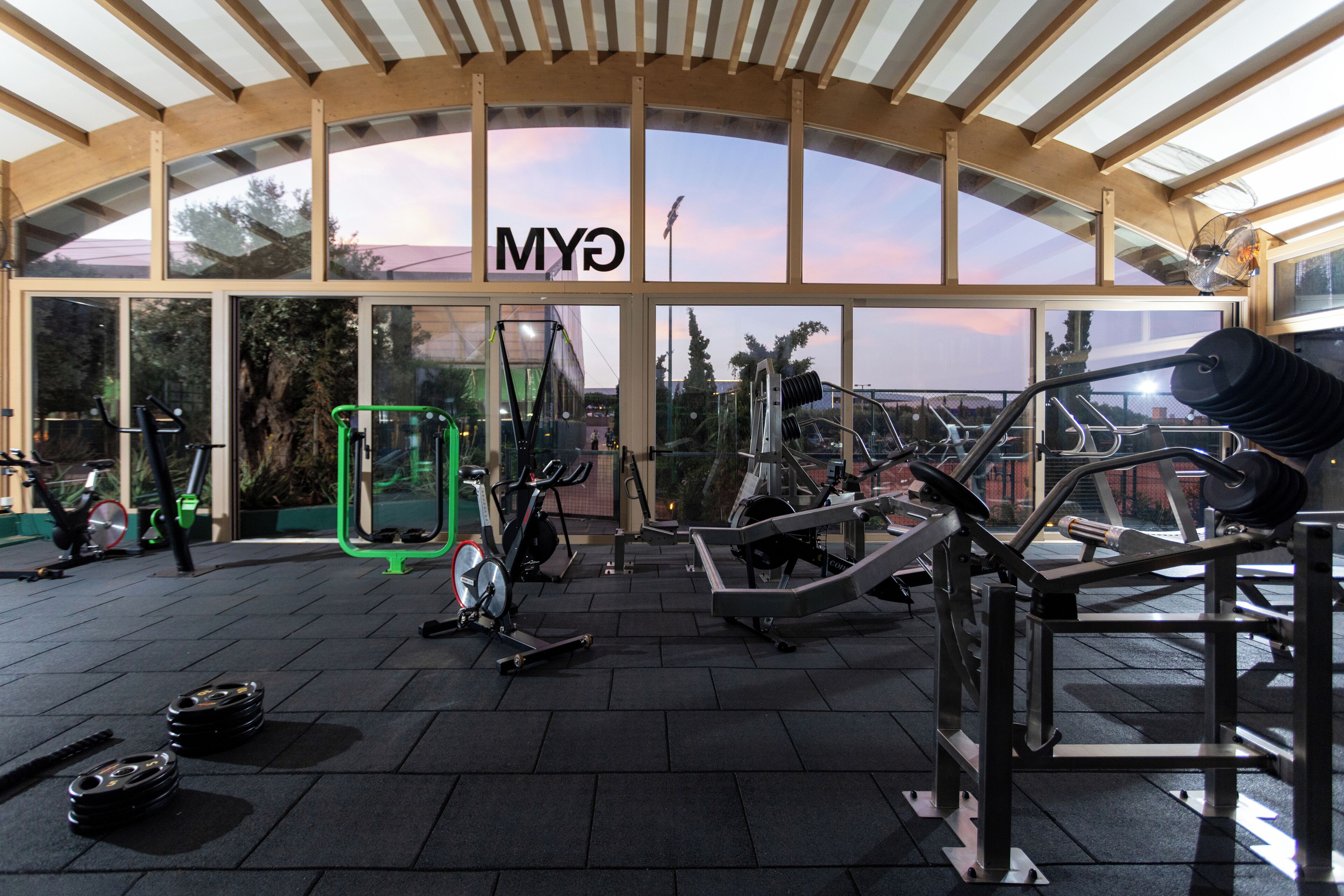 A gym with various exercise equipment, a large window with the letters 'MY' visible, and a covered roof structure.