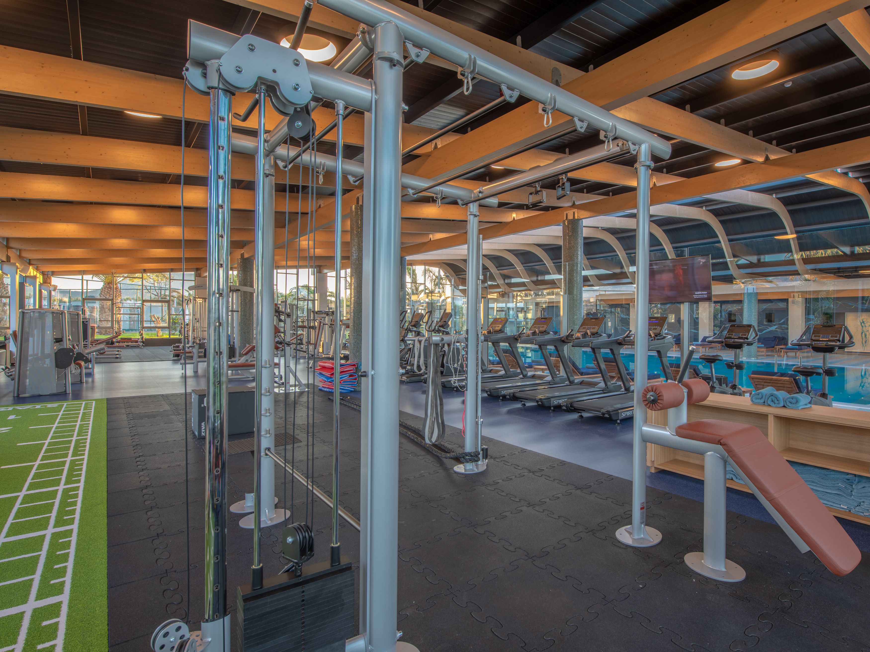 A gym with various exercise equipment, including treadmills and weight machines, under a high ceiling with natural light.
