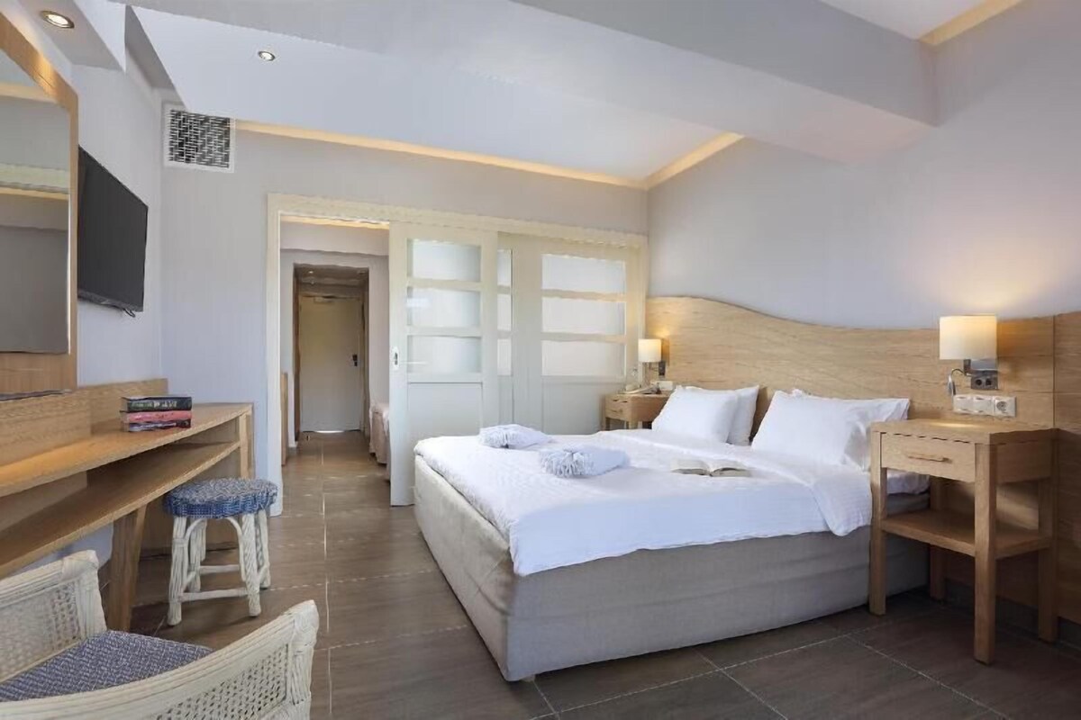 A bedroom with a bed, bedside tables, a desk, a chair, and a TV.