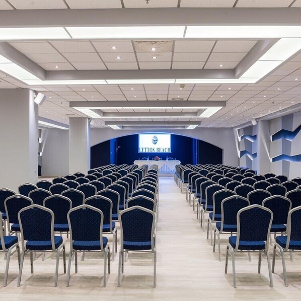 A conference room with rows of blue chairs facing a stage with a blue backdrop and the text "LYTTO'S BEACH".