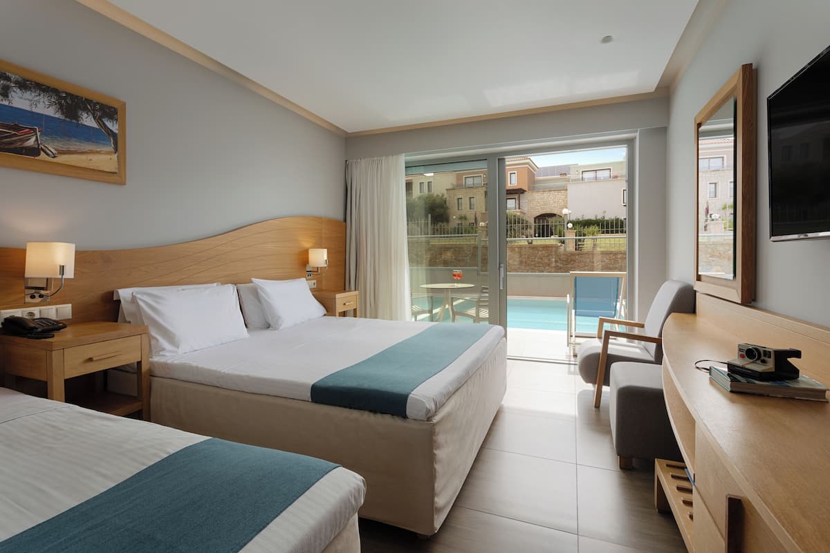 A hotel room with a bed, a desk, a chair, a TV, and a balcony with a pool.