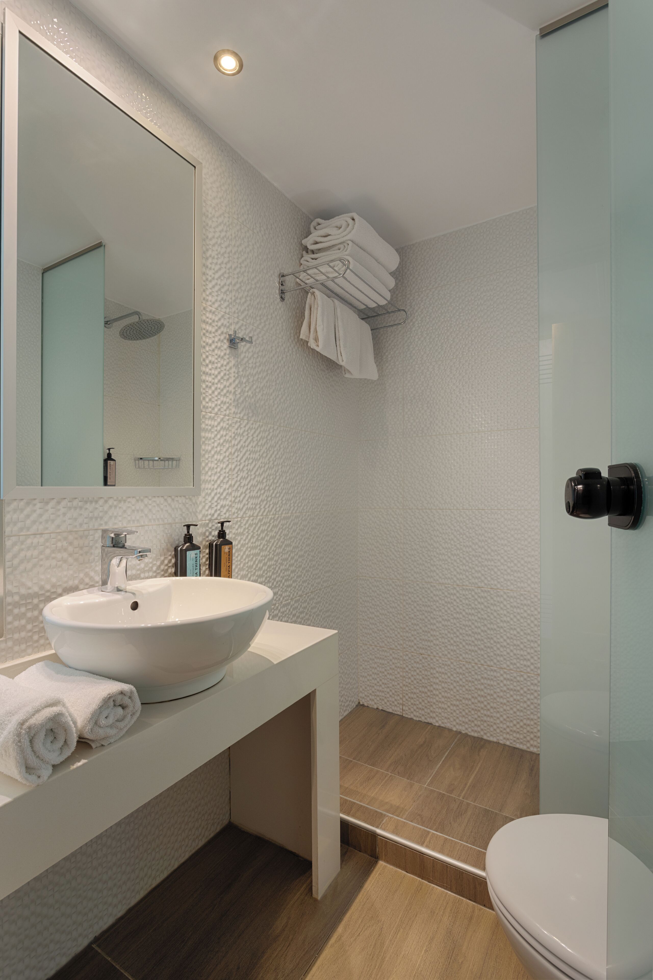 A modern bathroom with a white sink, mirror, and glass shower enclosure.