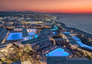 Un resort con una amplia piscina, varias opciones de restaurantes y vistas al océano al atardecer.