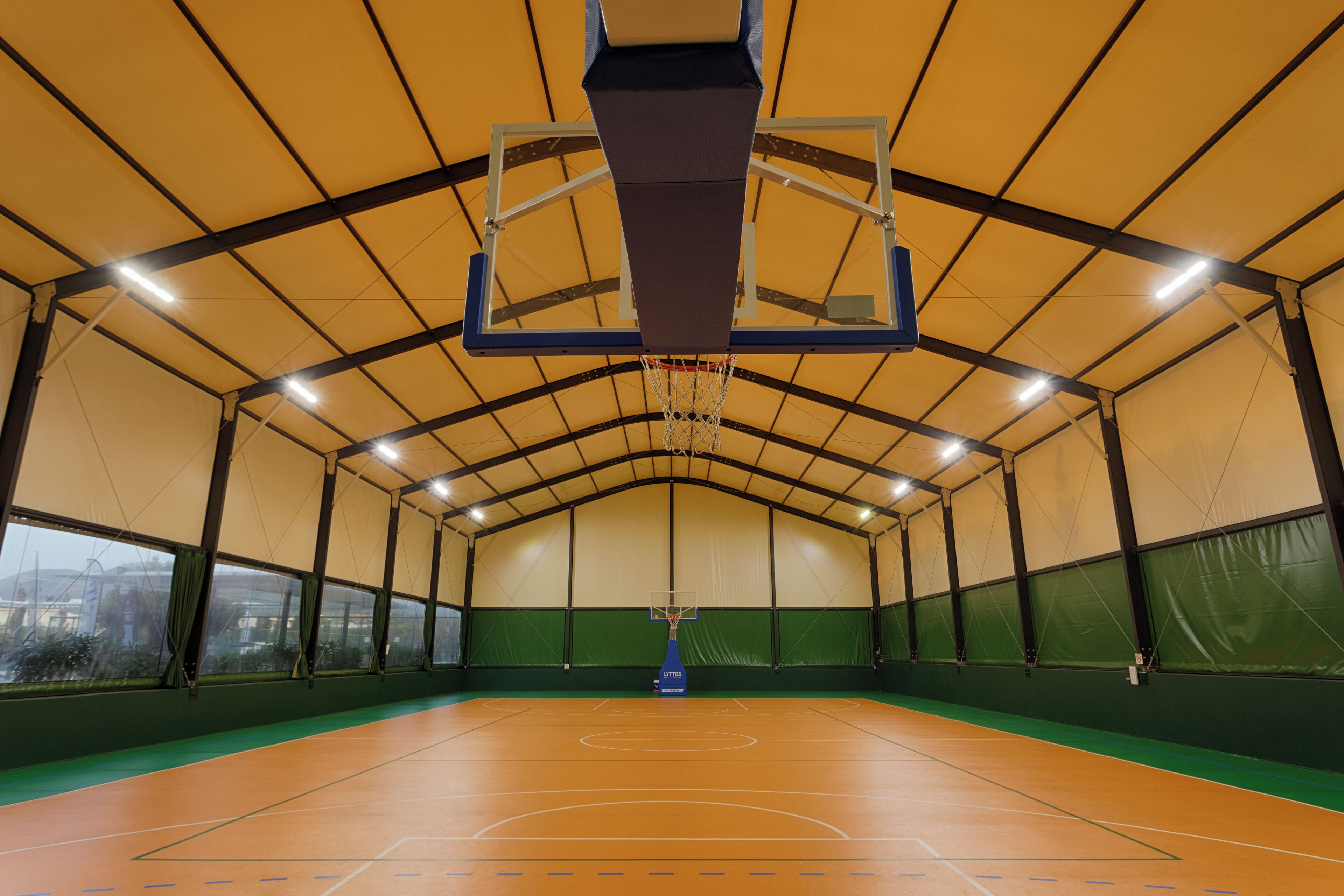 Una cancha de baloncesto cubierta con red, paredes verdes y un techo alto.