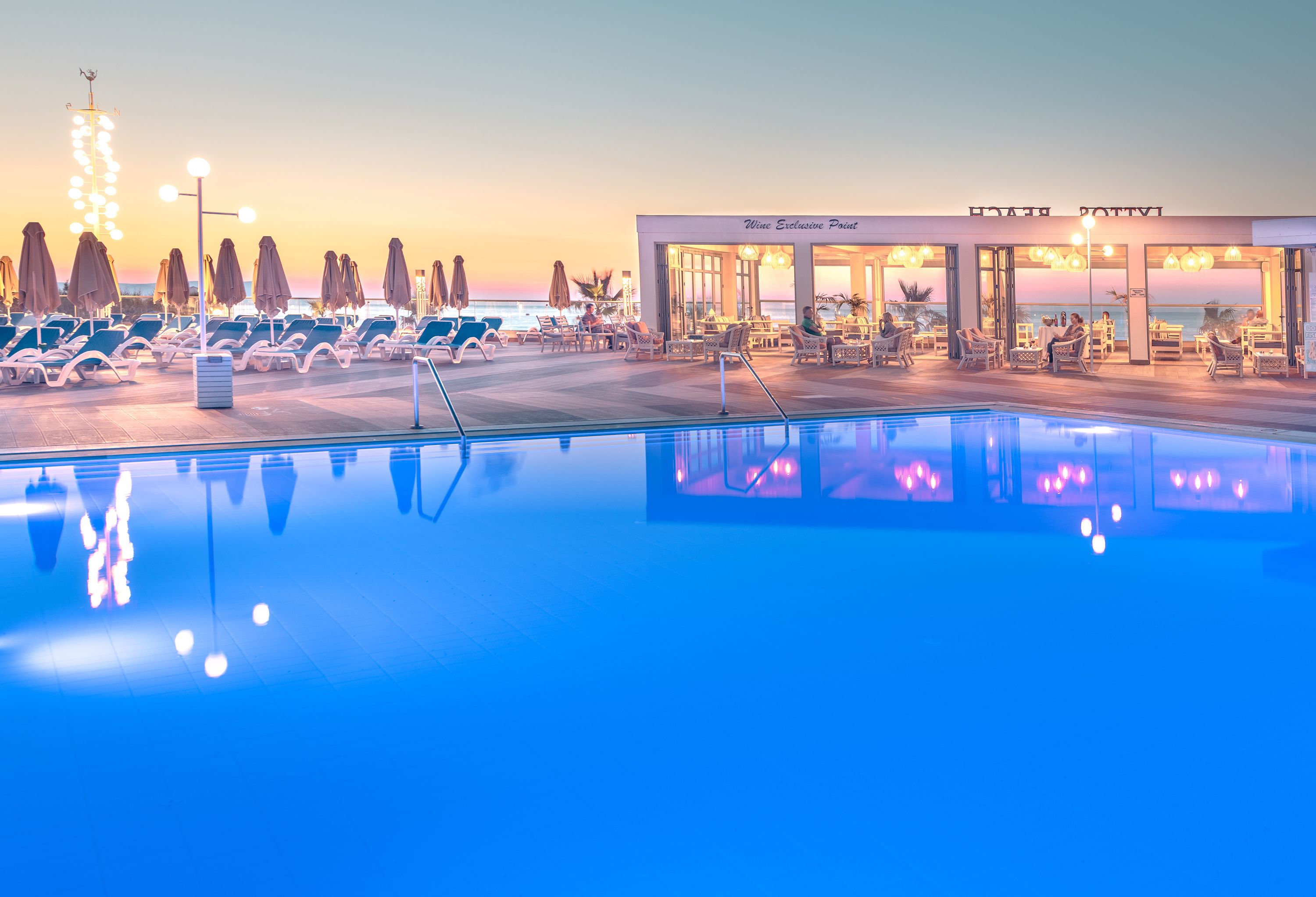 Zona junto a la piscina con sillones de descanso y un restaurante llamado Wine Exclusive Point.