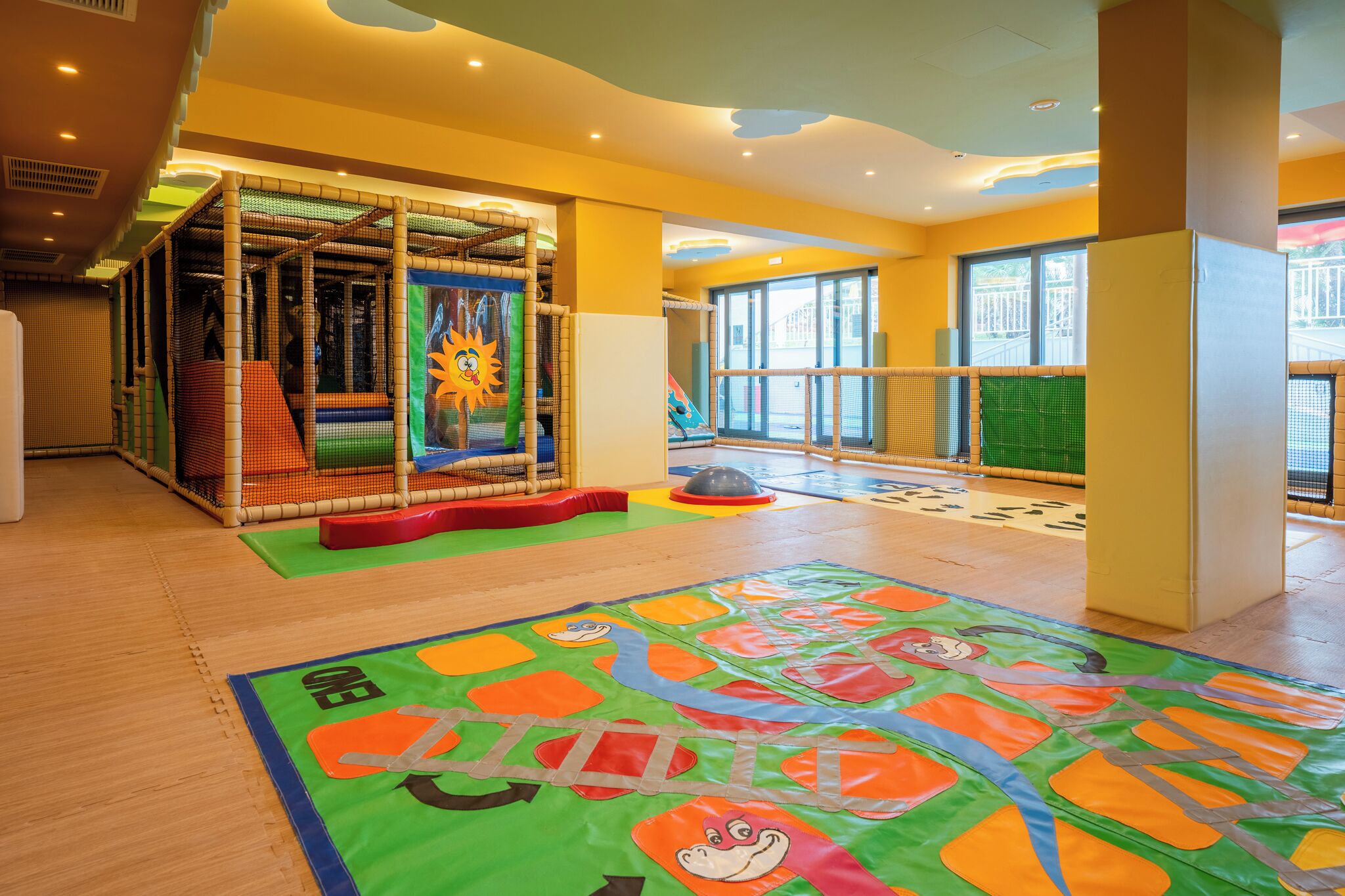 A children's play area with a soft play structure, a colorful mat, and a large window.