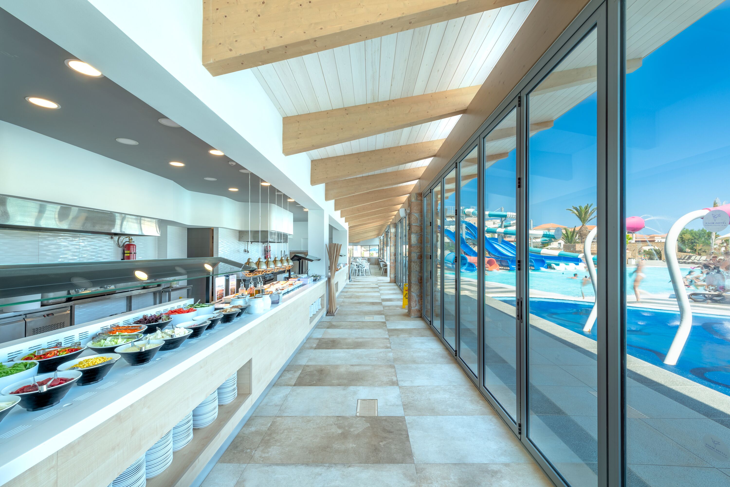A buffet with various food items, a pool area with slides, and a clear view of the resort's architecture.