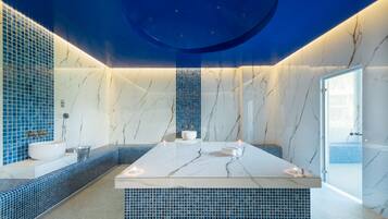 Bathroom features a central island, white sink, and toilet, set against a blue-tiled backdrop.