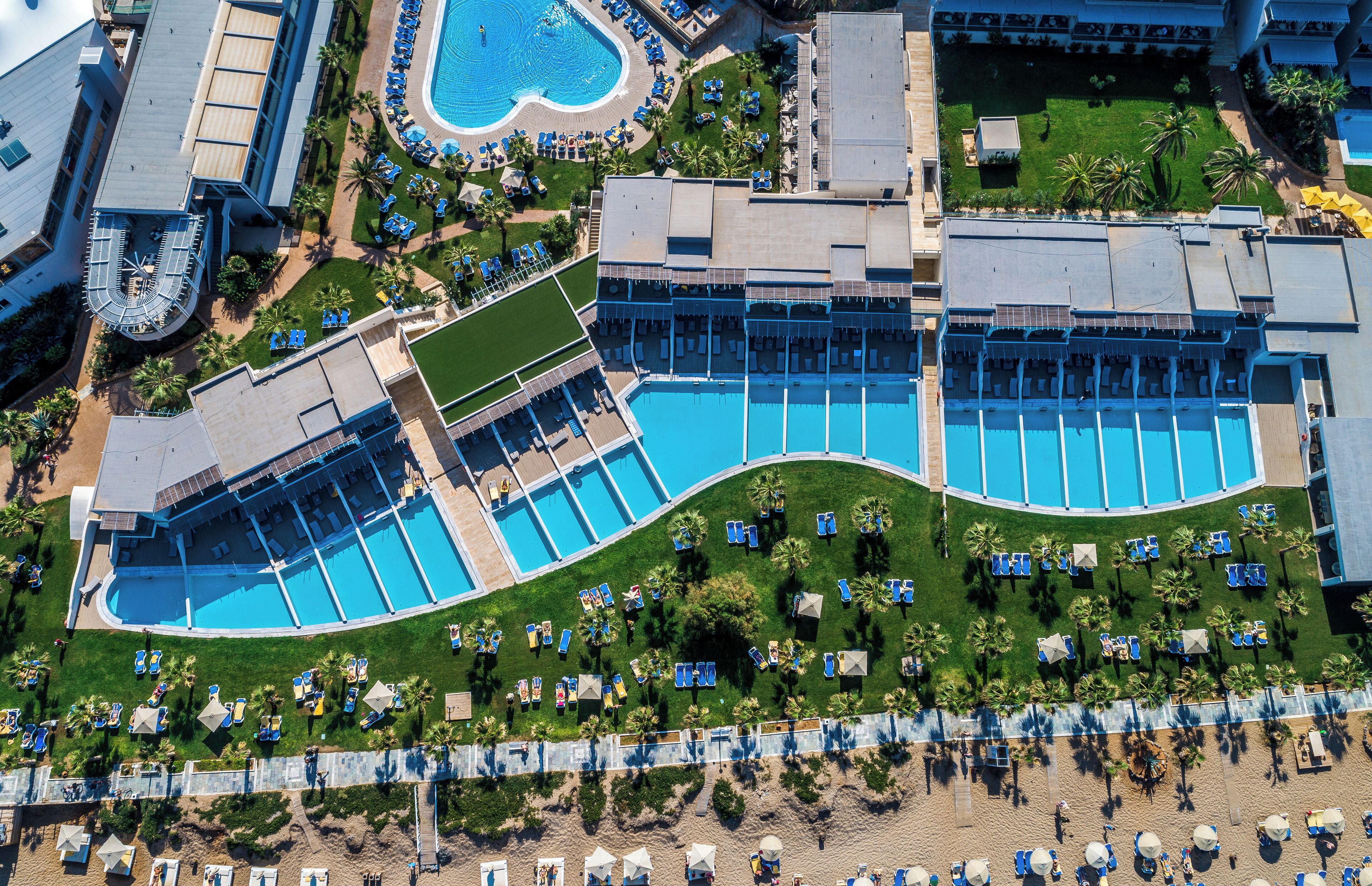 An aerial view of a resort with multiple swimming pools, sun loungers, and palm trees.