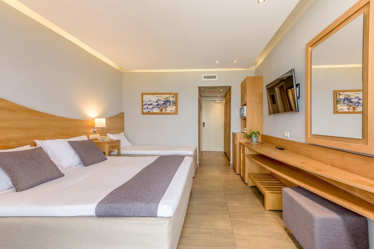 A hotel room with two beds, a TV, a desk, and a mirror.