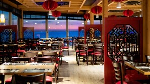 Ein Restaurant mit Holztischen und -stühlen, roten Laternen und traditionellen chinesischen architektonischen Elementen.