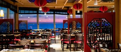 Um restaurante com mesas e cadeiras de madeira, lanternas vermelhas e elementos arquitetônicos tradicionais chineses.
