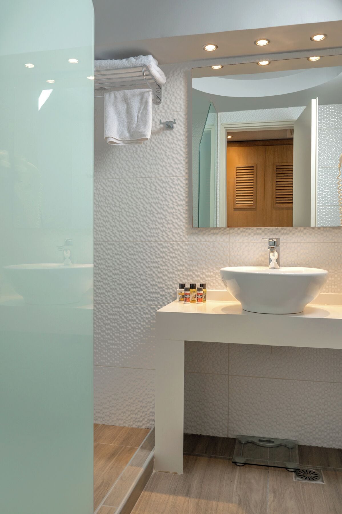 Un baño moderno con un lavabo blanco, un espejo grande y una cabina de ducha de vidrio.