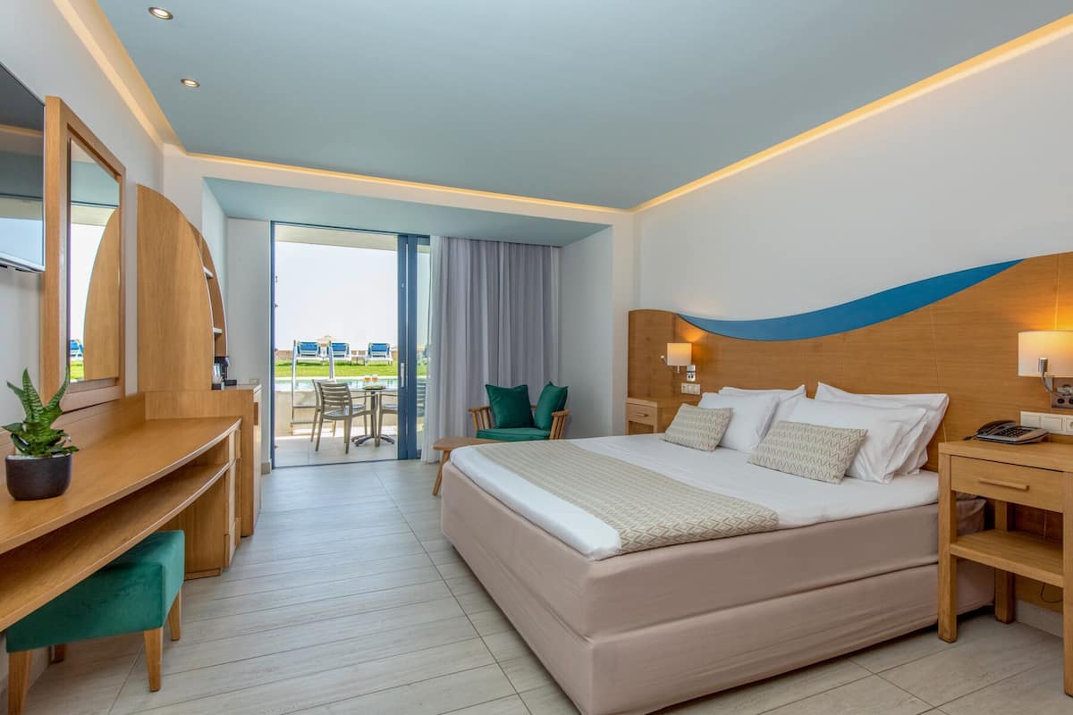 A modern hotel room with a large bed, a desk, a chair, and a view of the outdoor area.