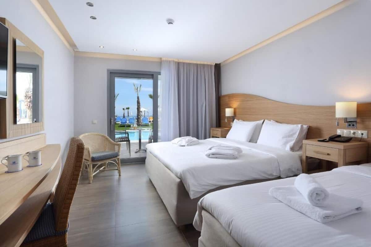 A hotel room with two beds, a desk, a chair, a TV, and a view of a pool.