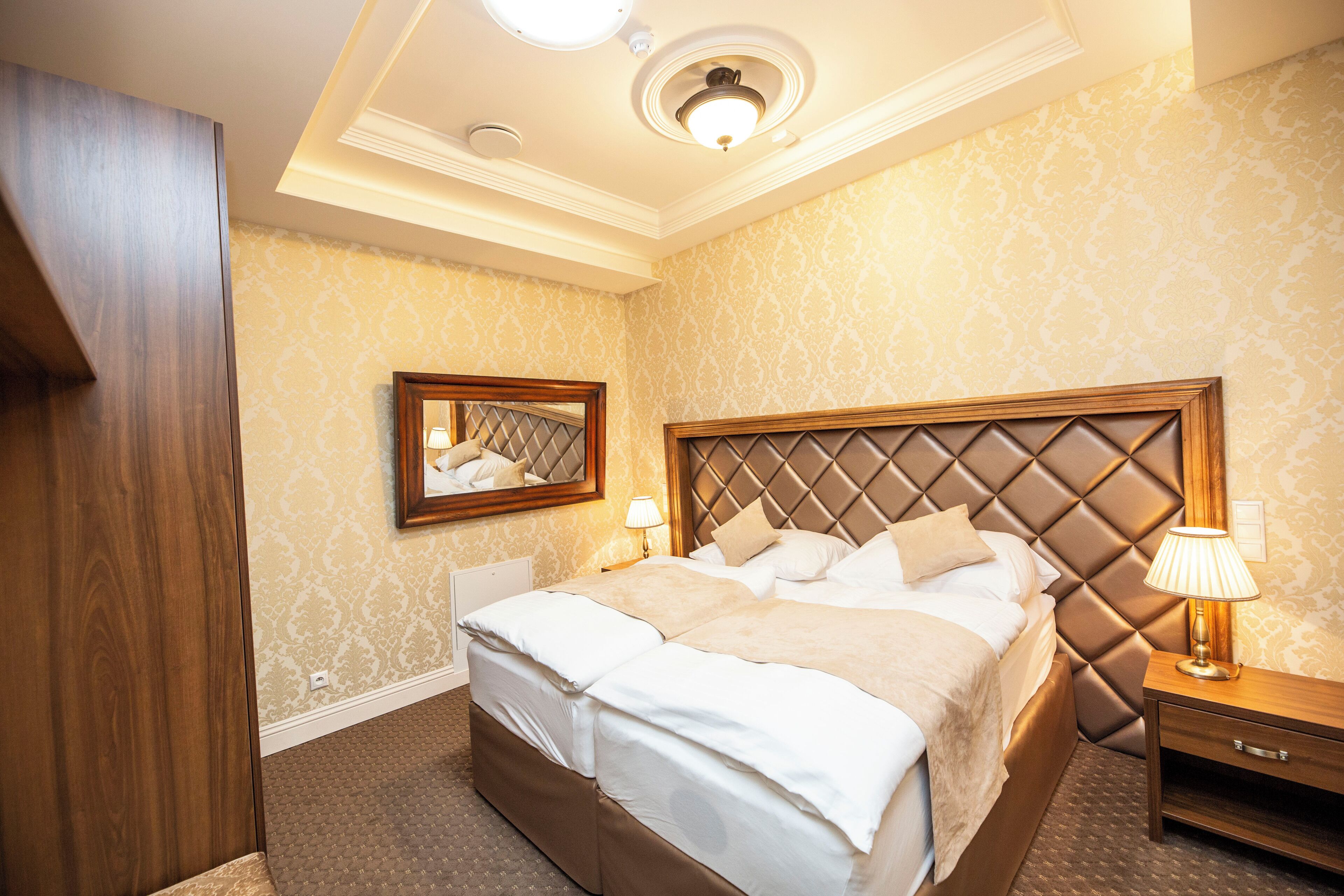 A hotel room with a large bed, a nightstand, a mirror, and a ceiling light.