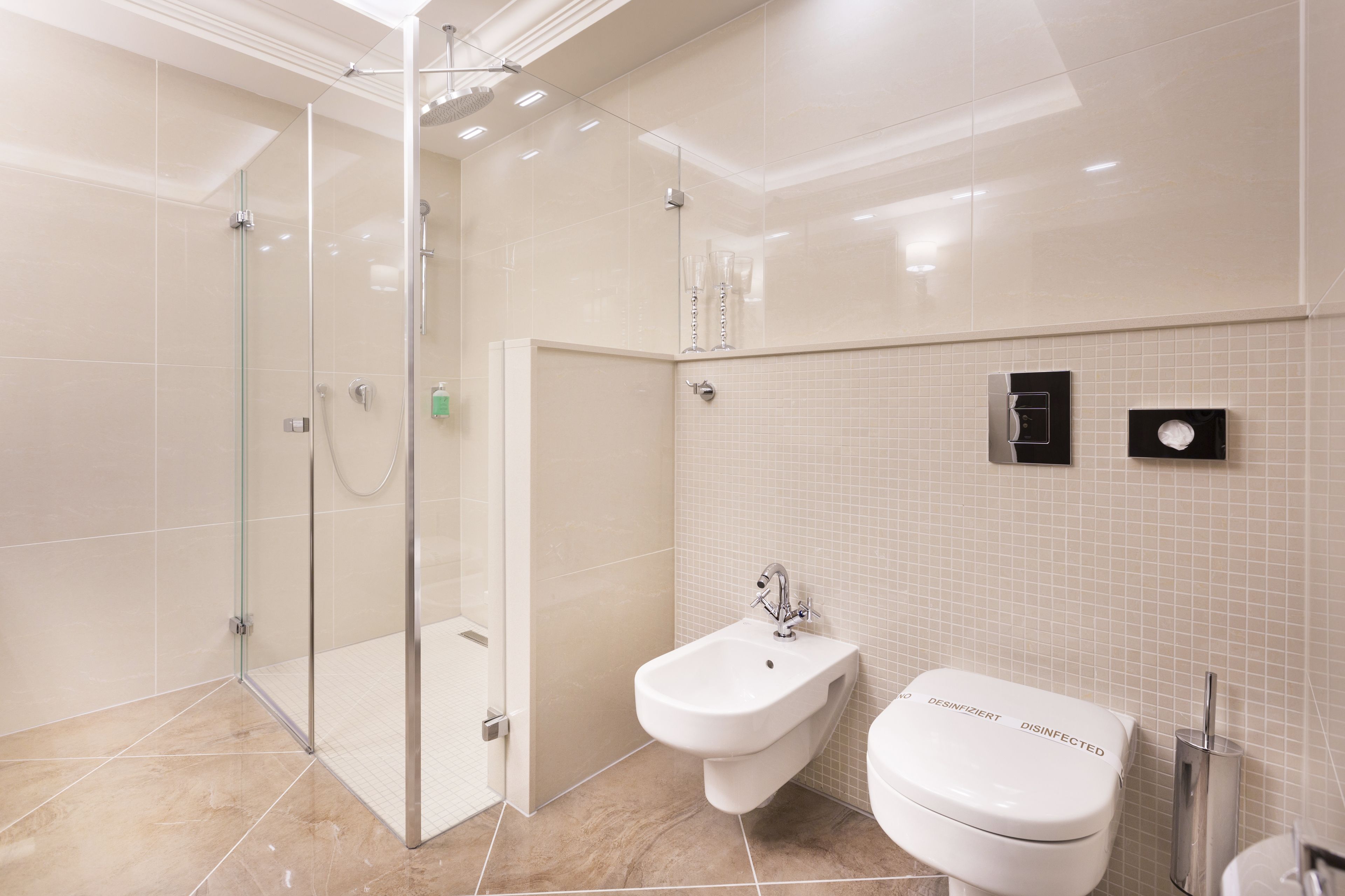 Et moderne badeværelse med et brusebadekar i glas, en bidet og et toilet med desinficeringsmærke.