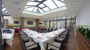 Un comedor amplio con largas mesas dispuestas para varios invitados, con un techo alto con tragaluces y vistas al exterior.