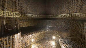 Un spa moderno con un diseño geométrico de mosaicos, una zona de estar con asientos curvos y un cabezal de ducha visible.