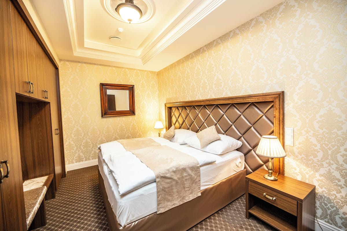 Quarto de hotel com uma cama grande, um guarda-roupa de madeira, uma mesa de cabeceira com abajur e um espelho na parede.
